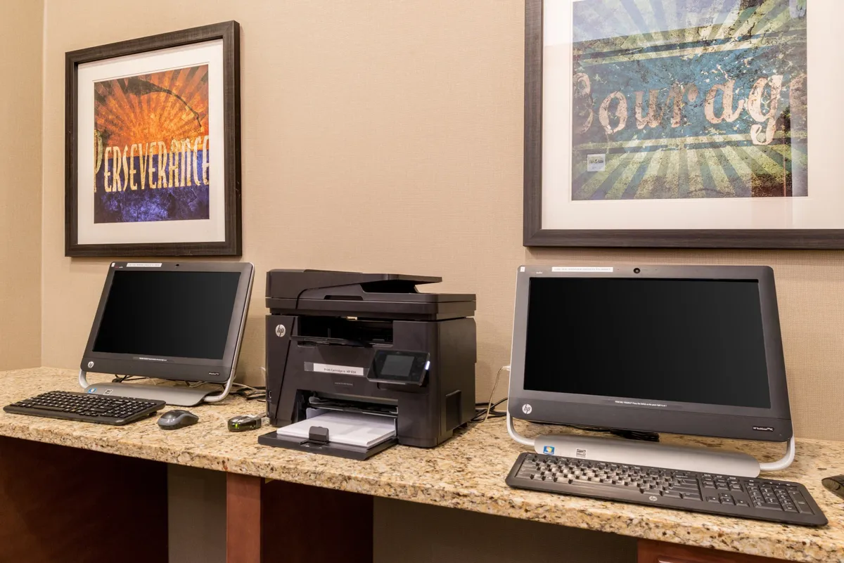 A productive workspace area with computers, a printer, and motivational artwork on the walls. The environment is bright and organized, ideal for business work, creative tasks, or catching up on emails.