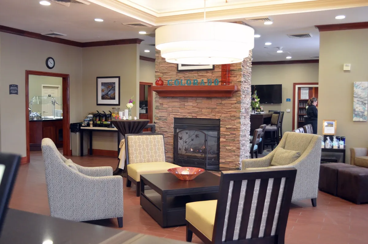 A cozy indoor lounge featuring a central fireplace, comfortable seating, and tasteful artwork. The arrangement invites guests to gather for social events, casual conversations, or quiet relaxation.