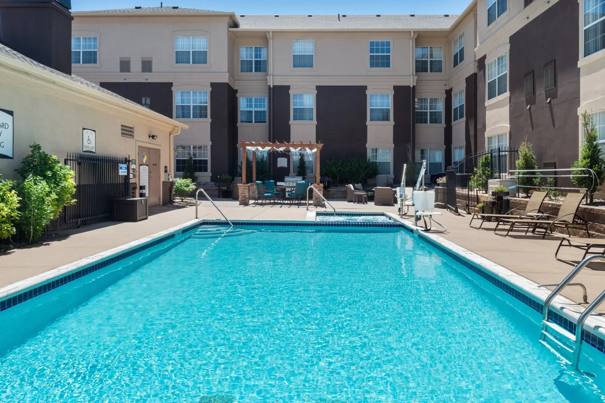 This image features the serene swimming pool area with comfortable lounge chairs and outdoor seating, situated against the modern facade of the hotel. The scene is peaceful, with guests sunbathing, swimming, or enjoying quiet moments by the water.