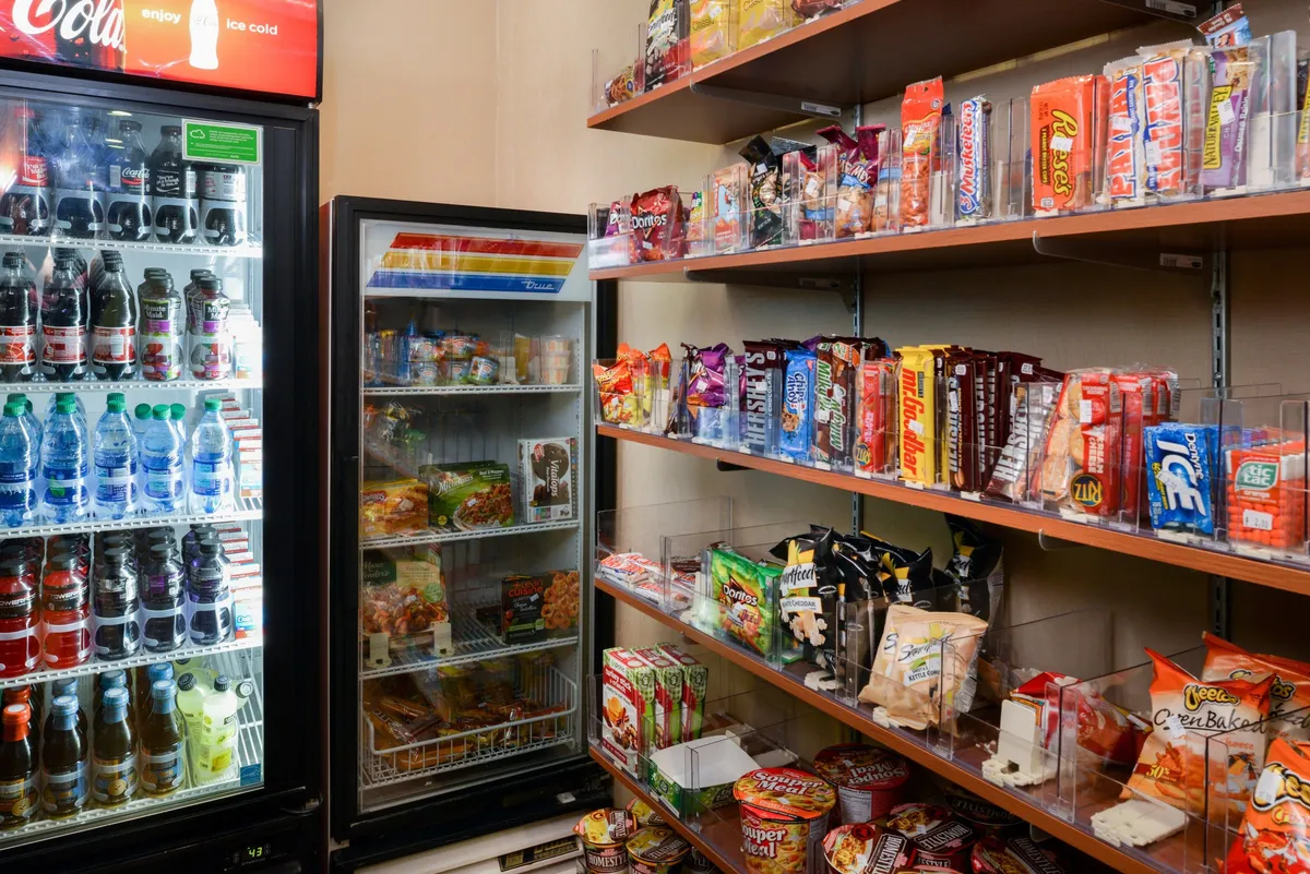 The image shows shelves fully stocked with snacks and a beverage fridge, offering a variety of quick bites and drinks. The setup is casual and convenient, perfect for spontaneous snack breaks or light refreshments between meals.