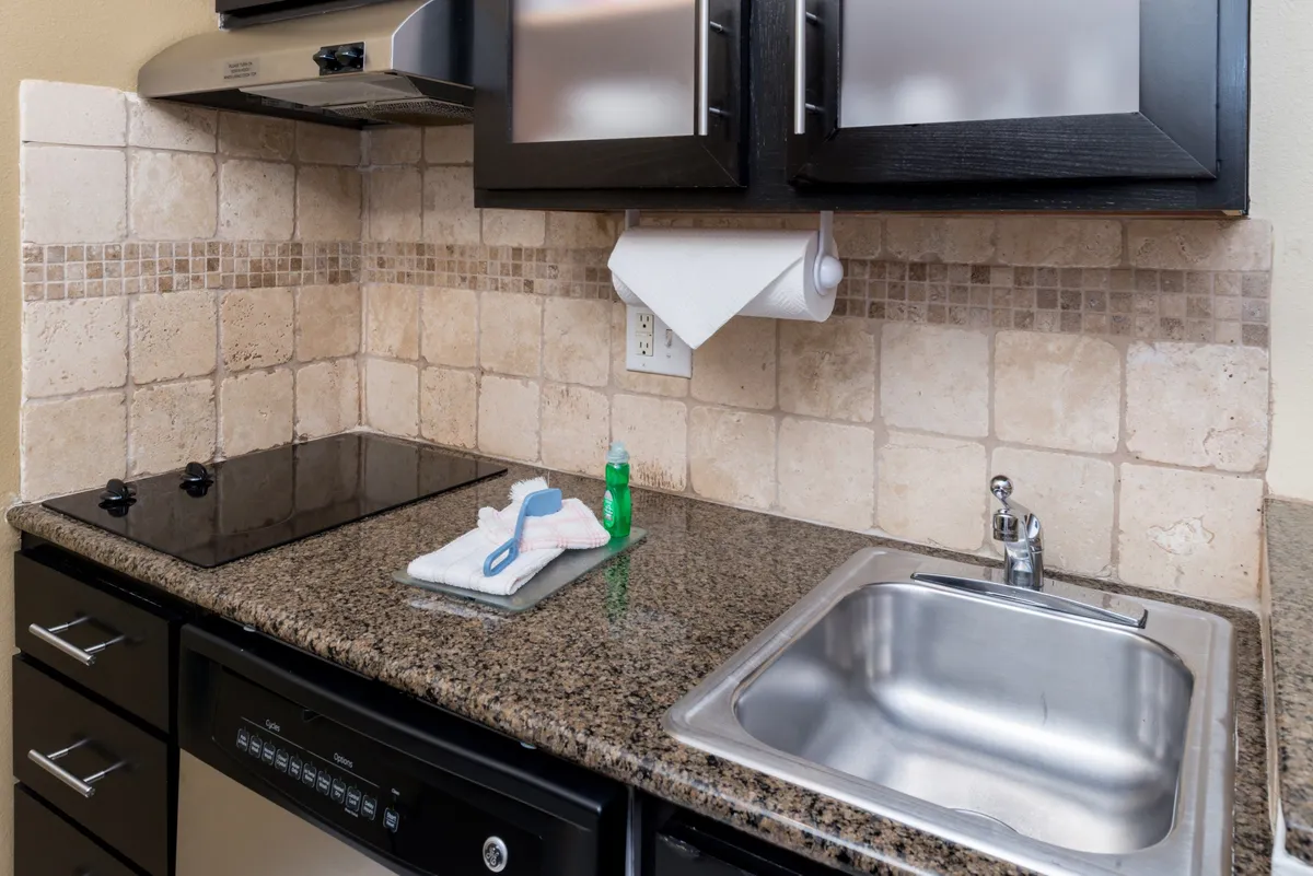This image captures a modern kitchen space with black cabinetry, a sleek granite countertop, modern appliances, and a textured tile backsplash. The scene is set for cooking, entertaining, or preparing meals, suggesting a practical yet inviting environment for culinary activities.