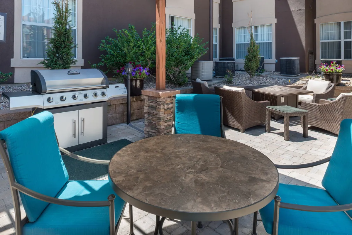 An inviting outdoor area with a grill, tables, and chairs set amidst lush greenery. The setting is ideal for relaxed gatherings, shared meals, and casual conversations, giving a sense of community and family enjoyment.